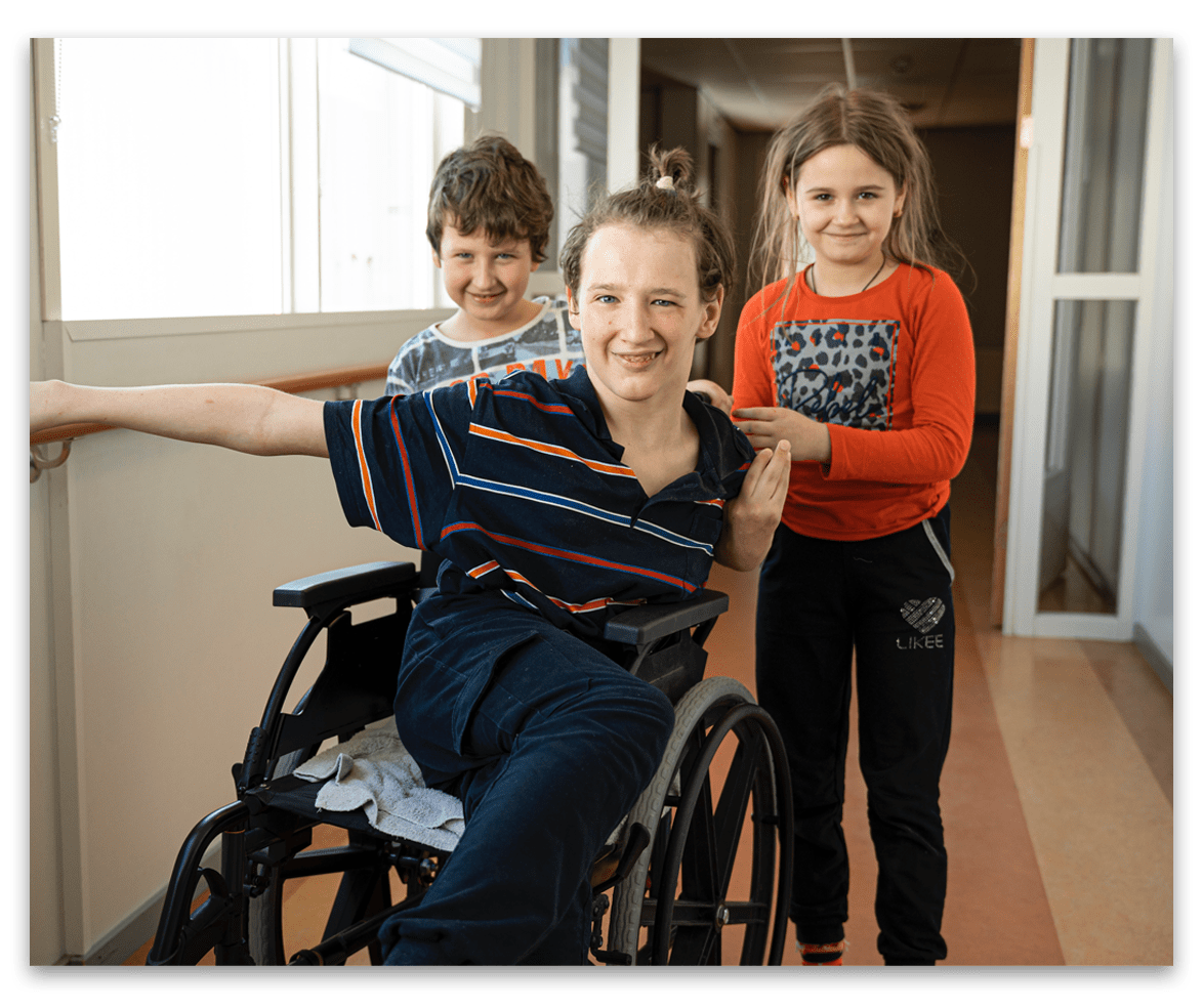 Image of a child in a wheelchair, with two children standing behind.